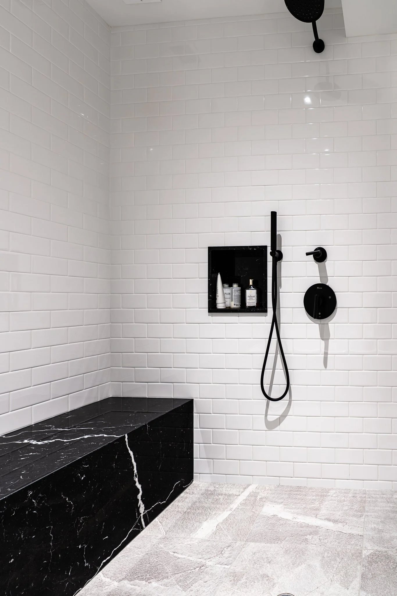 Modern walk-in shower with white subway tiles, black fixtures, a black marble bench, and a gray textured floor.