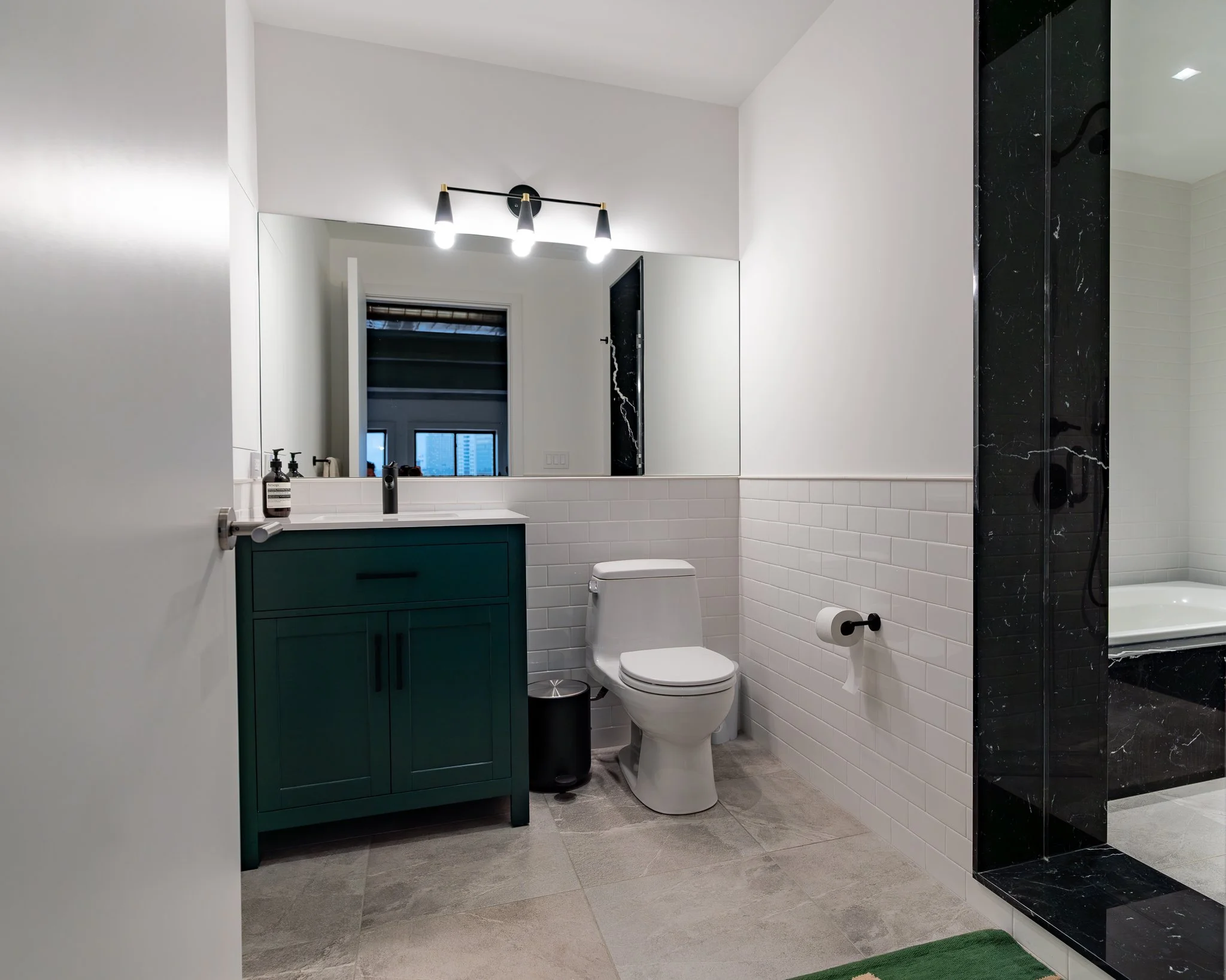 Modern bathroom with a teal vanity, white subway tile walls, a toilet, black marble shower, and large mirror.