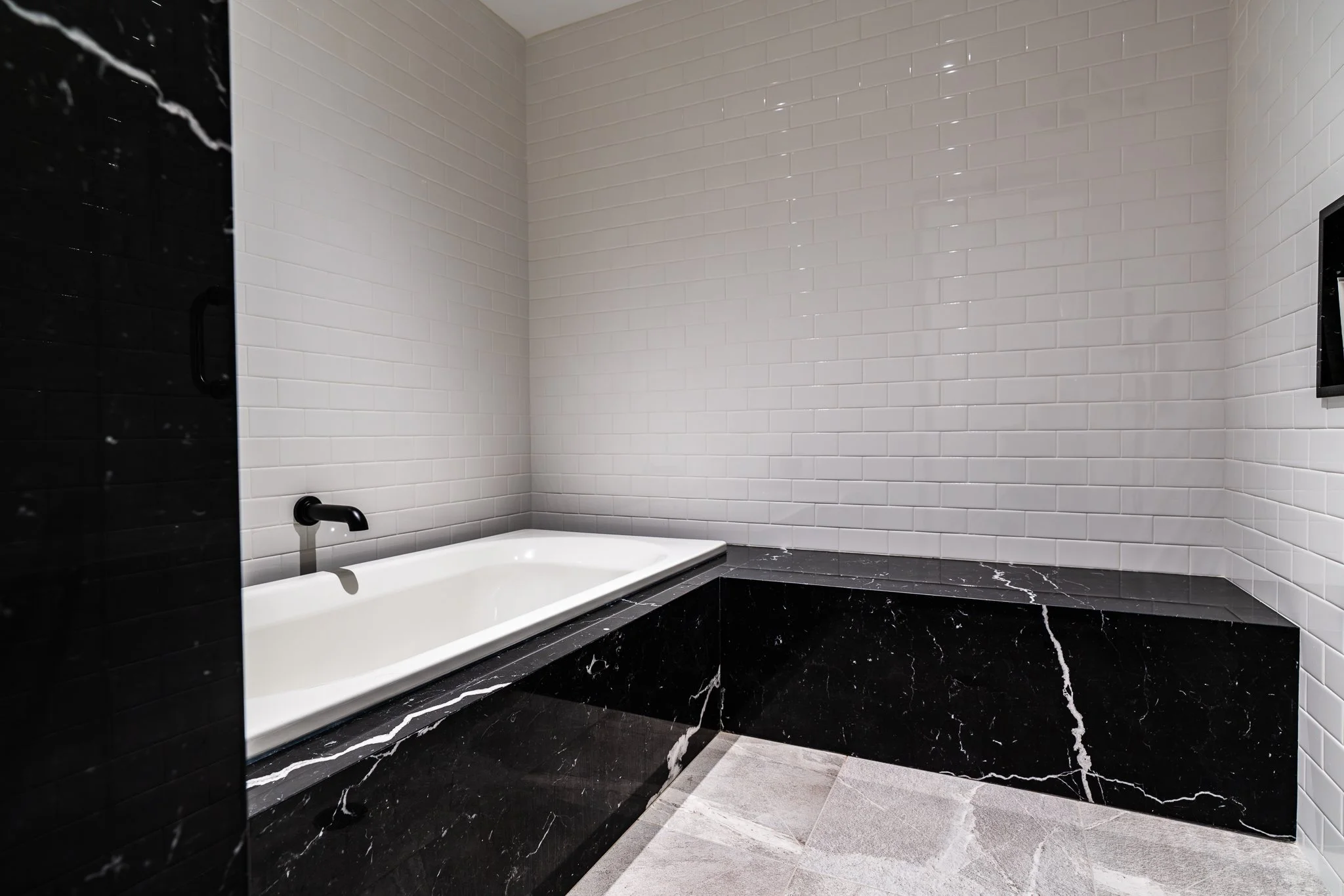 Modern bathroom with black marble countertop, white subway tile walls, and a built-in bathtub.