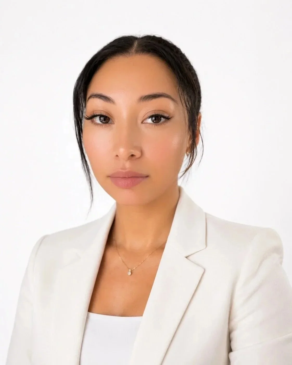 Portrait of a woman with dark hair, light makeup, and wearing a white blazer and a delicate necklace, against a plain white background.
