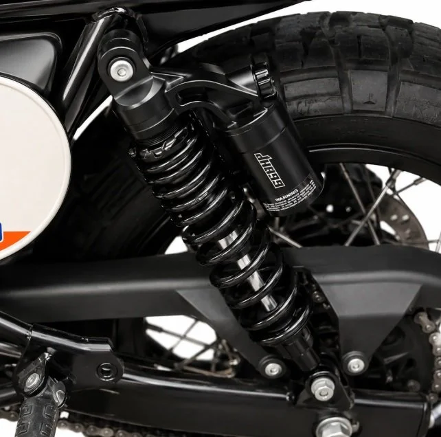 Close-up of a motorcycle's rear suspension with a black coil shock absorber and a large rear tire.