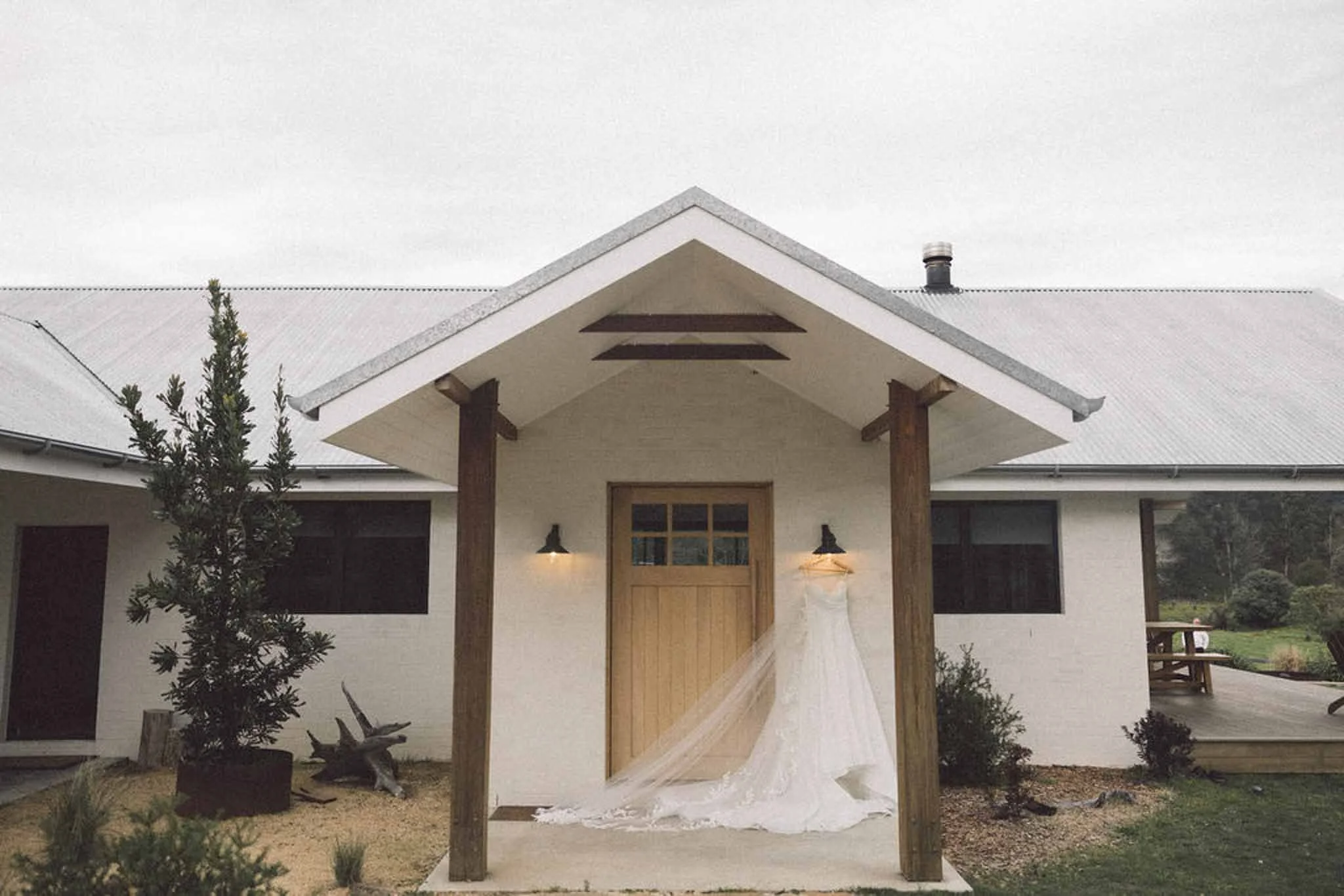 A bride and groom holding hands and walking outside a house on their wedding day, with the bride in a white wedding dress and the groom in a dark suit.