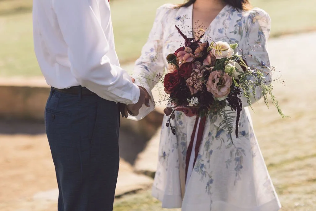 Outdoor view of a wedding altar decorated with flower arrangements on a wooden platform, overlooking a grassy field with trees in the distance.