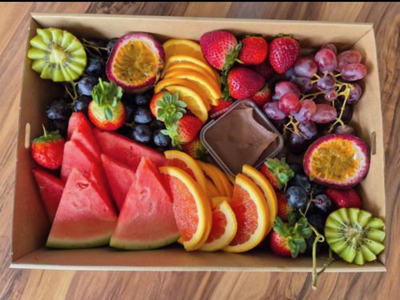 A box of fresh fruit including a chocolate dipping sauce.