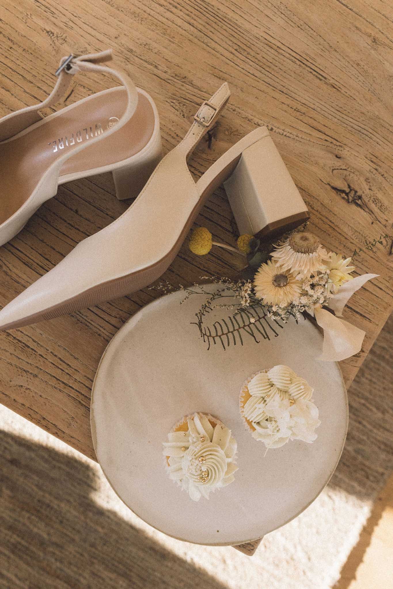 Close-up of a pair of beige high-heeled shoes with ankle straps, placed on a wooden surface.