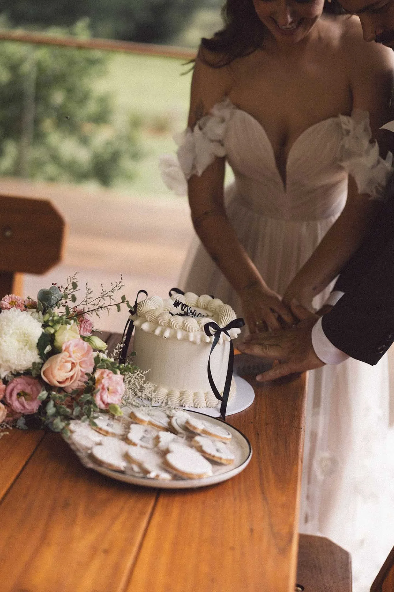 A couple exchanging rings at a wedding ceremony. A wedding cake with icing and ribbons, and a floral bouquet are on the table.