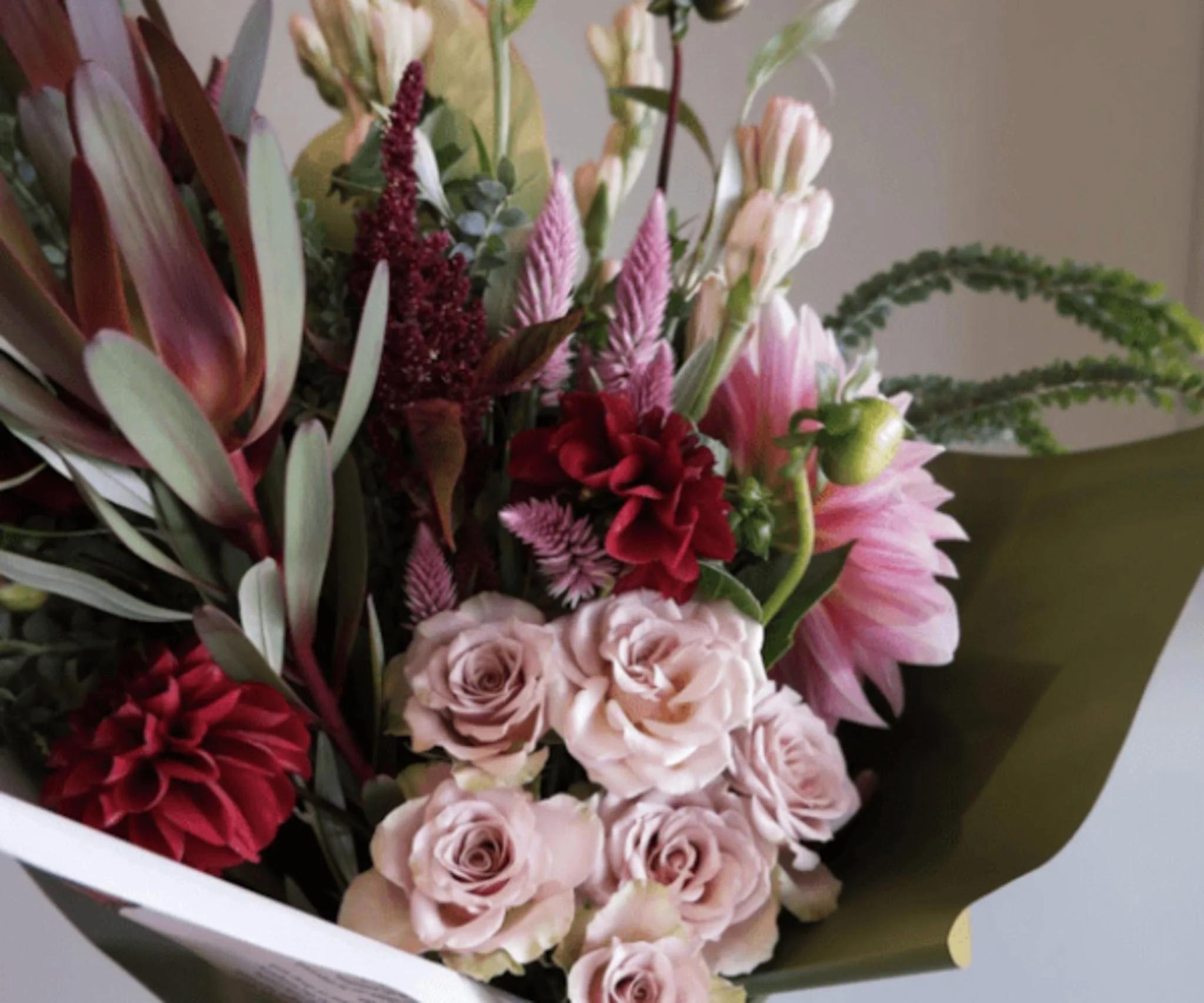 A bouquet of various pink and red flowers wrapped in white paper.
