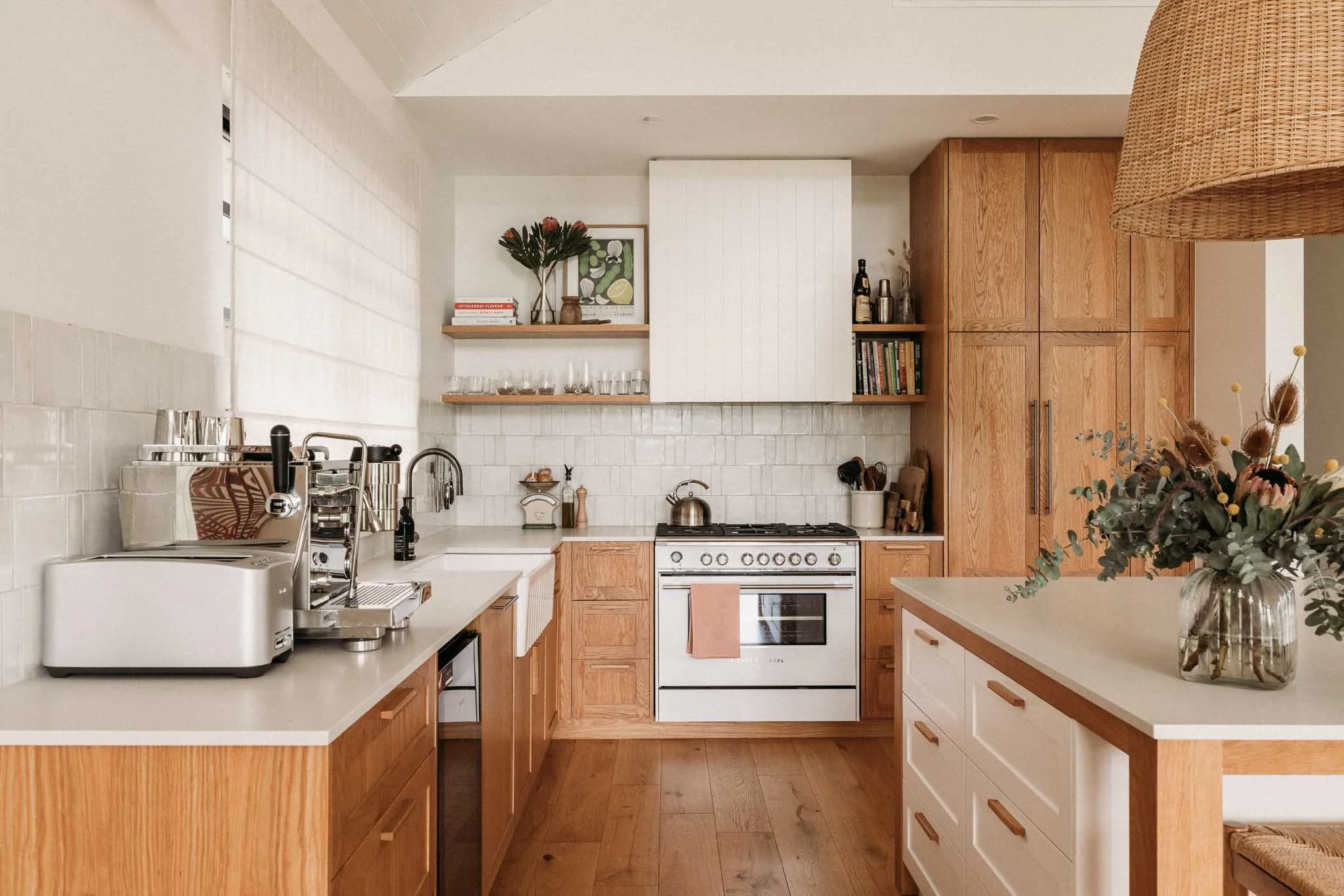 A cozy kitchen with wooden cabinets, white countertops, a gas stove, and a flower arrangement on the island.