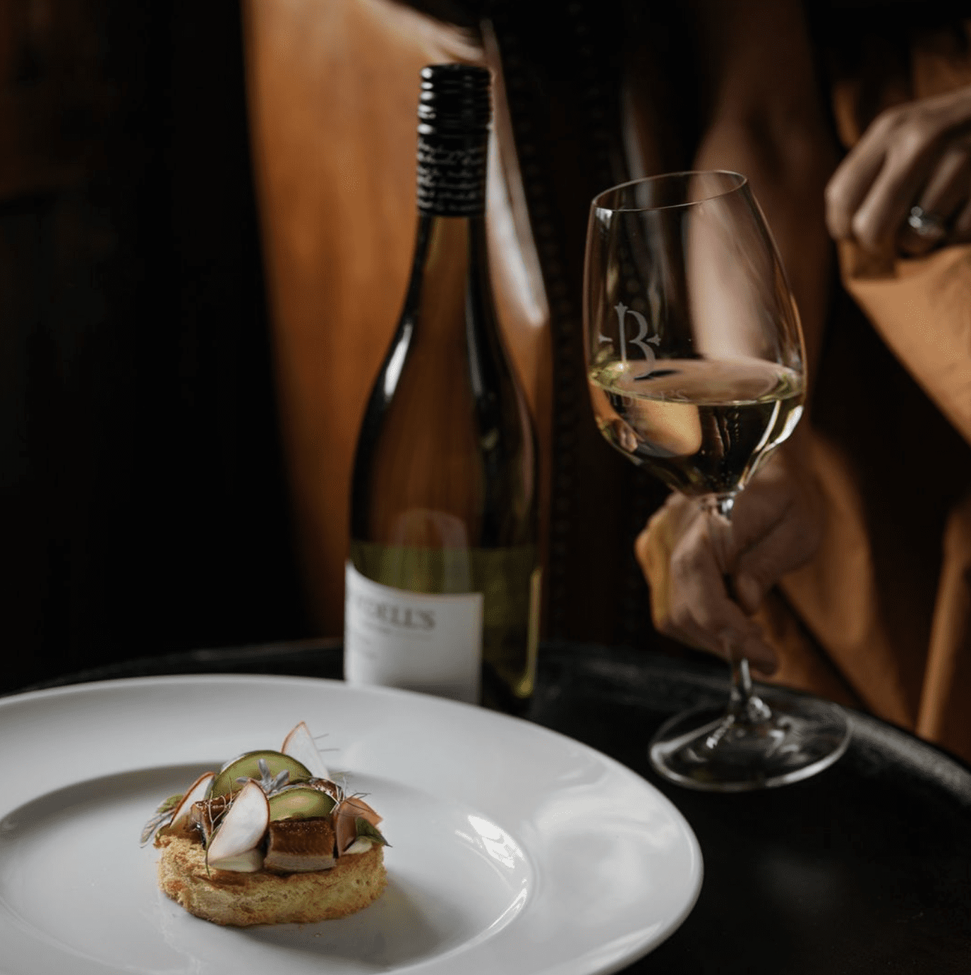 A dessert on a white plate with a wine glass and a wine bottle in the background.