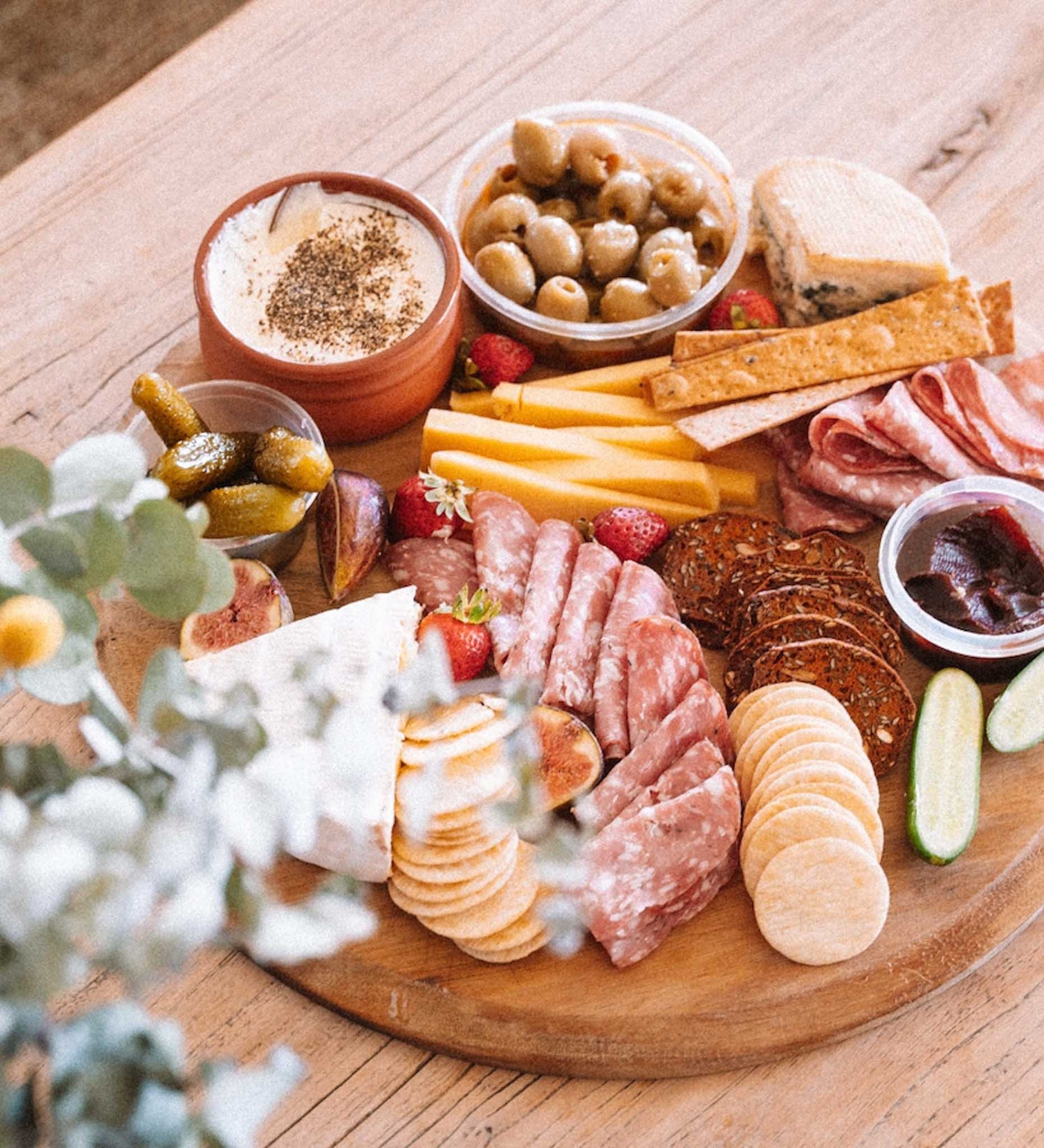 A charcuterie board with cheeses, meats, crackers, pickles, strawberries, and dips on a wooden surface.