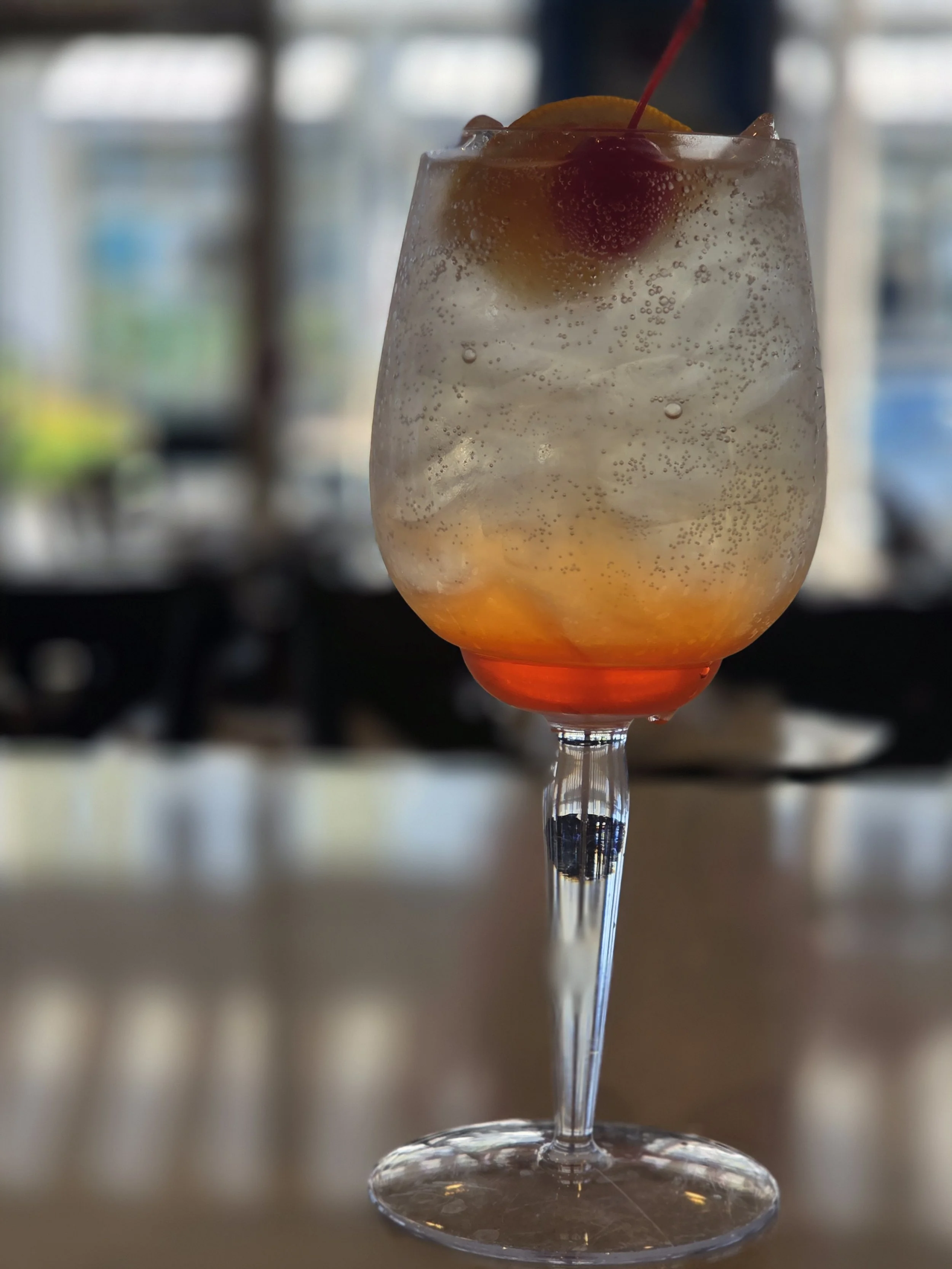 A tall glass filled with an Aperol Spritz. Aperol topped with prosecco and club soda. Garnished with an orange.