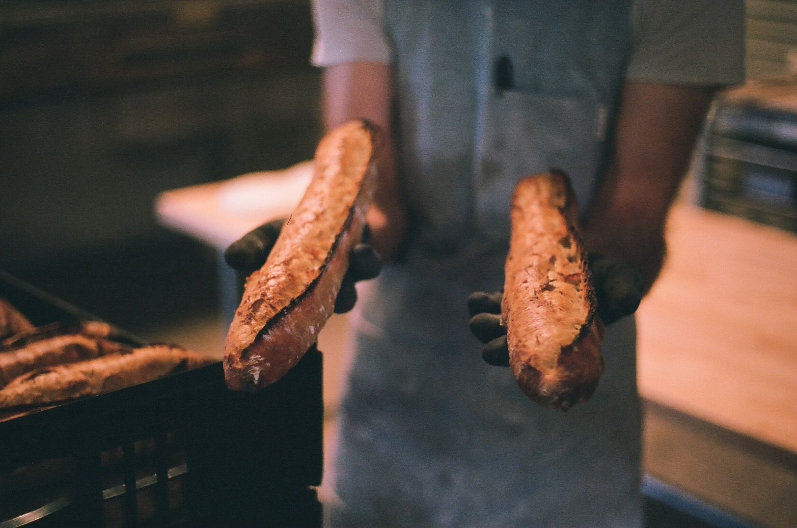 A person wearing a gray shirt holding two freshly cooked sweet potato fries, one in each hand, in a kitchen or food handling setting.