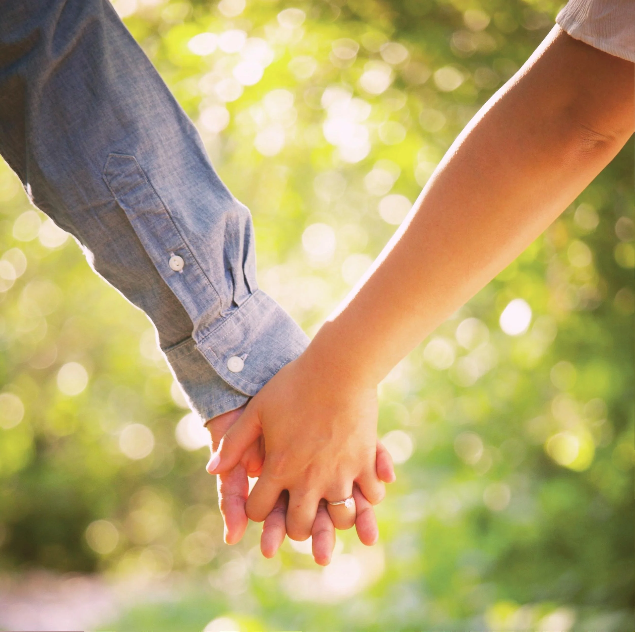 Two people holding hands outdoors in soft sunlight, representing connection and support