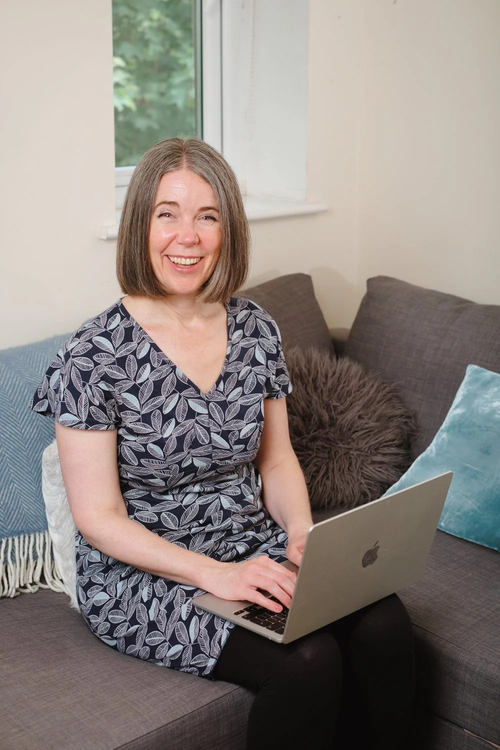 Nicola Pott, therapist, smiling while working on a laptop in a cosy counselling space