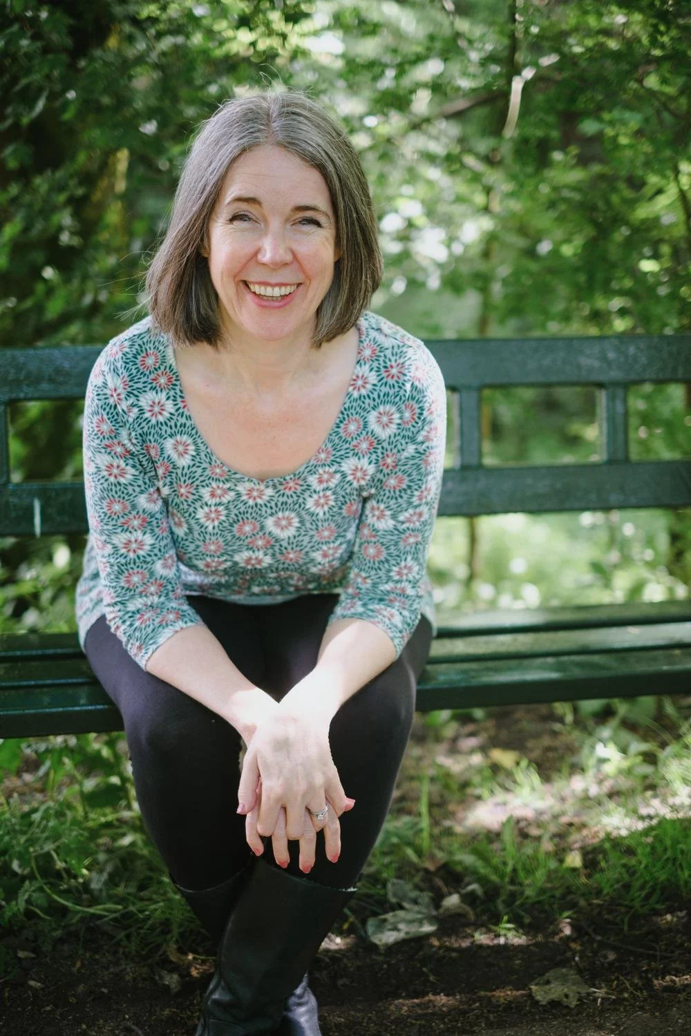 Nicola Pott, therapist, sitting on a garden bench smiling in a lush green park