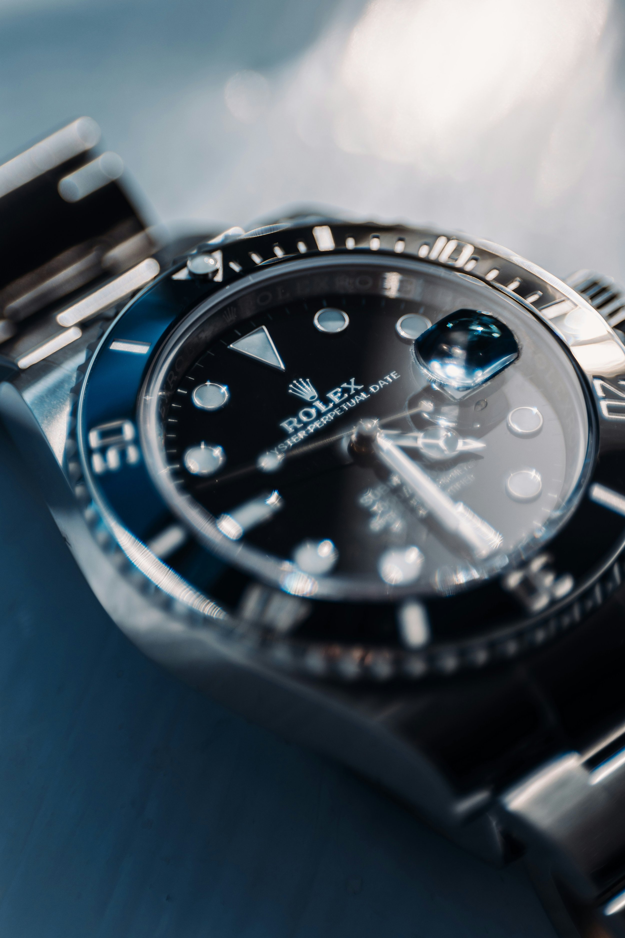Close-up of a Rolex watch with a black dial, silver bezel, and a date window, placed on a dark surface.