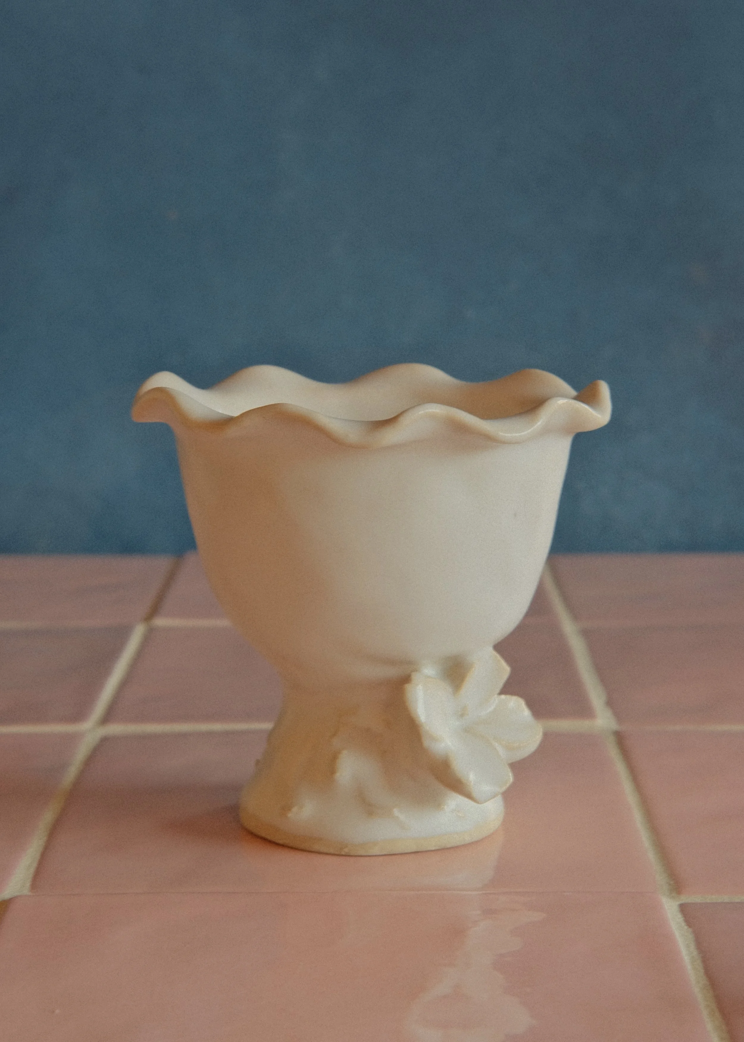 Porcelain vase with ruffled edges on a pink tiled surface against a blue background.