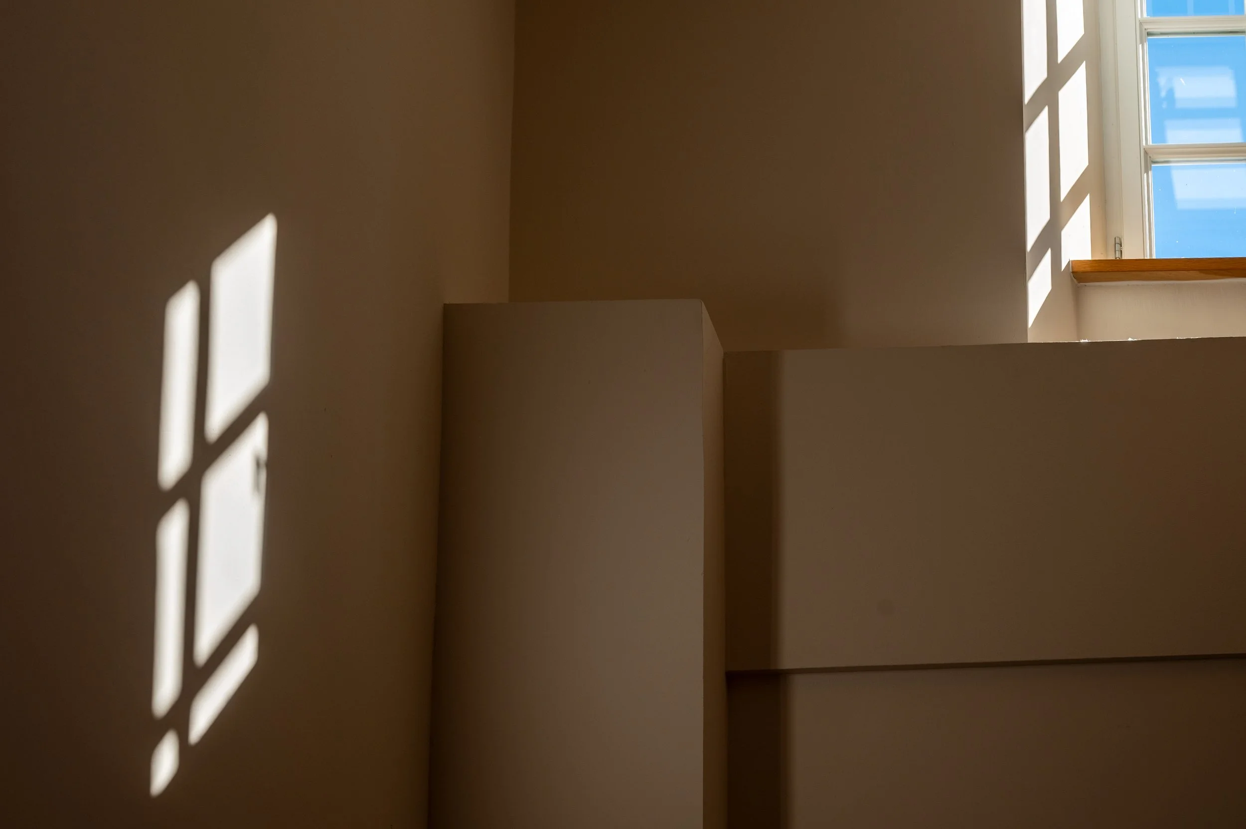 Sonneneinstrahlung durch ein Fenster wirft Schatten an die Wand, Fenster mit blauer Himmel im Hintergrund.