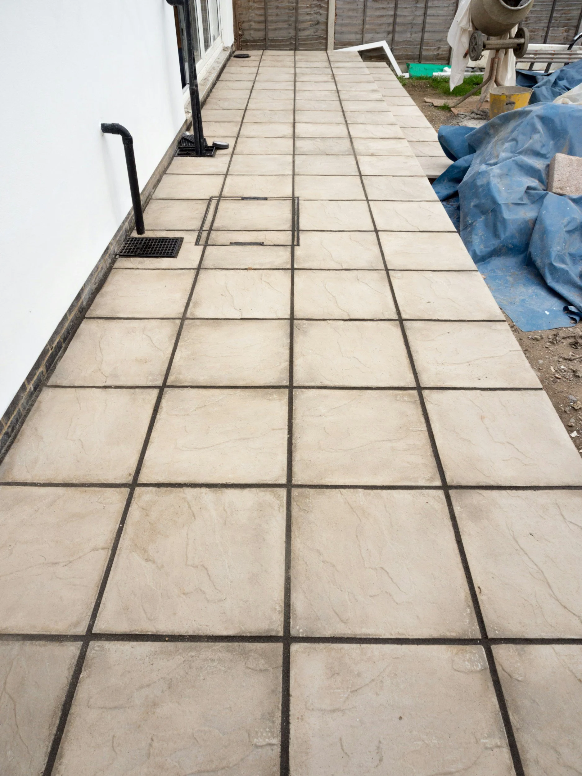 Construction site with a tiled patio area, partially completed, with construction materials and equipment around.