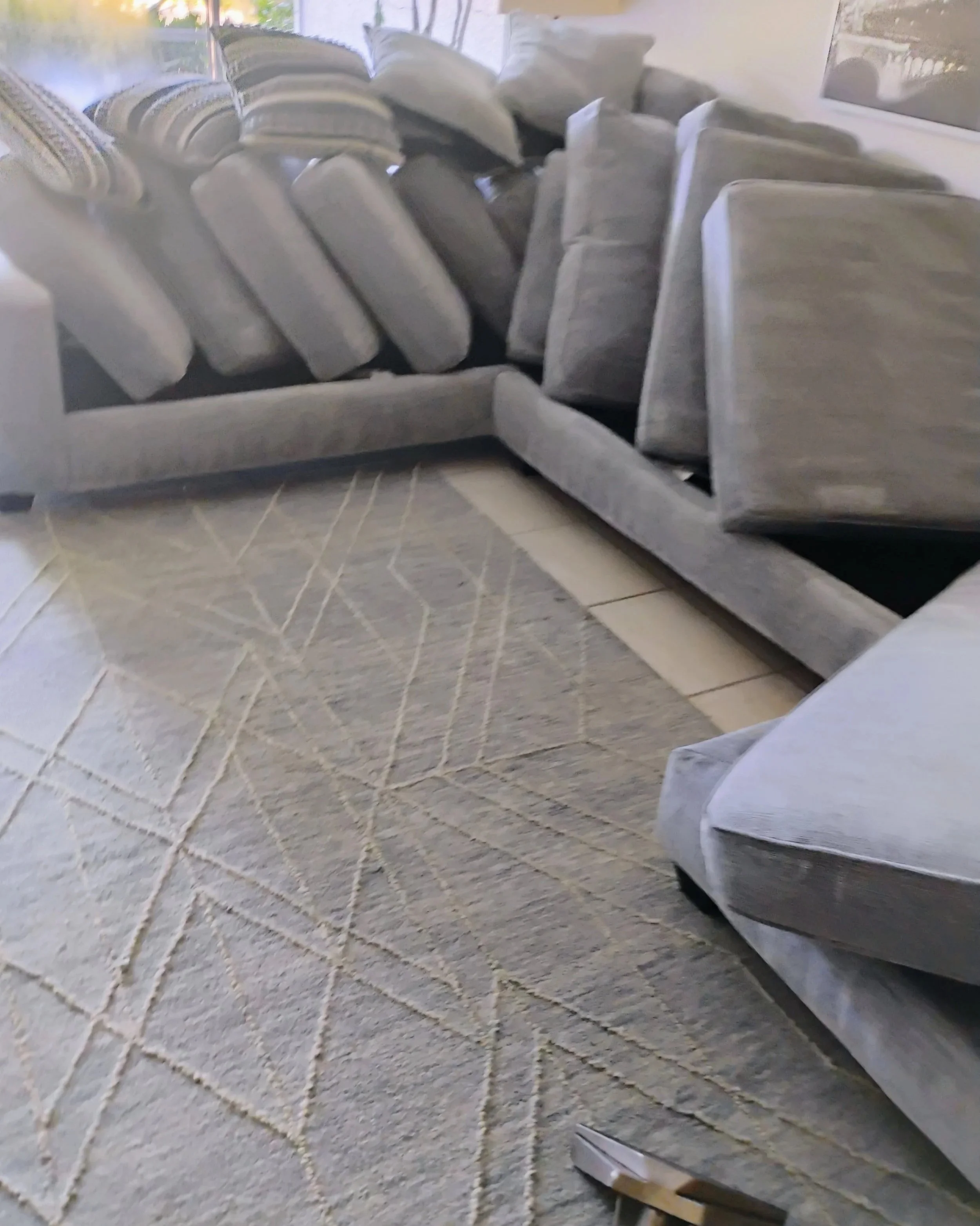 A stack of white and patterned cushions stacked on a couch near a wall with framed pictures, with a tiled floor underneath.