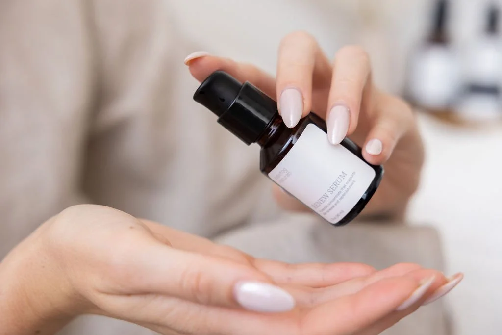 Person applying serum from a small bottle onto their hand in a skincare routine.