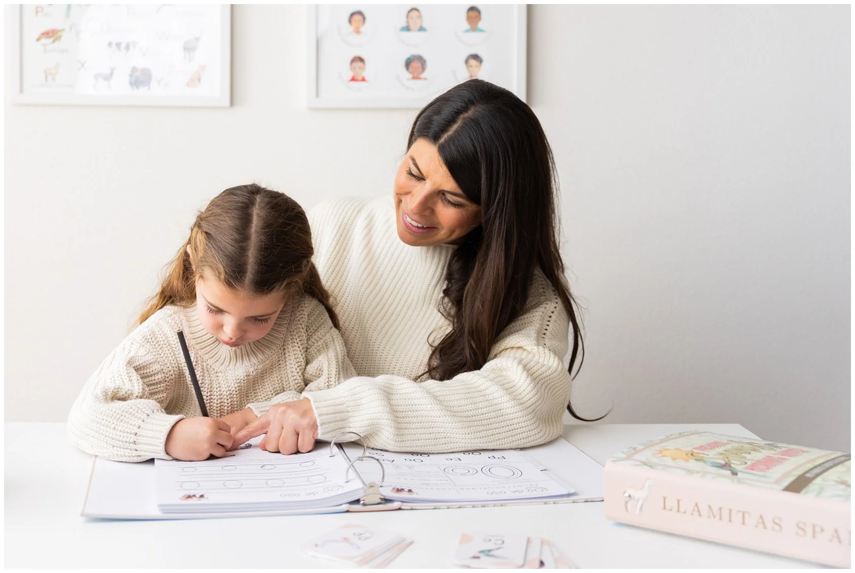 A woman helping a young girl with her homework at a table, with educational posters in the background.