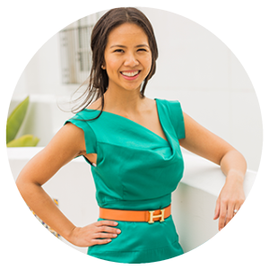 A woman smiling, wearing a teal dress with a yellow belt, standing outdoors.