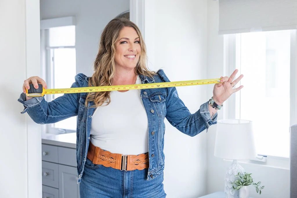 woman in denim jacket and jeans holding a measuring tape in a bright room