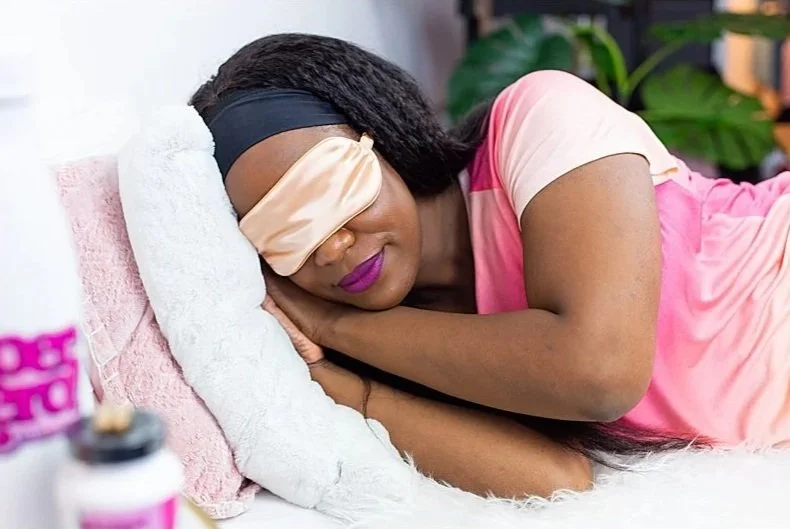 Woman resting her head on a pillow with an eye mask on, lying on her side, in a bedroom setting.
