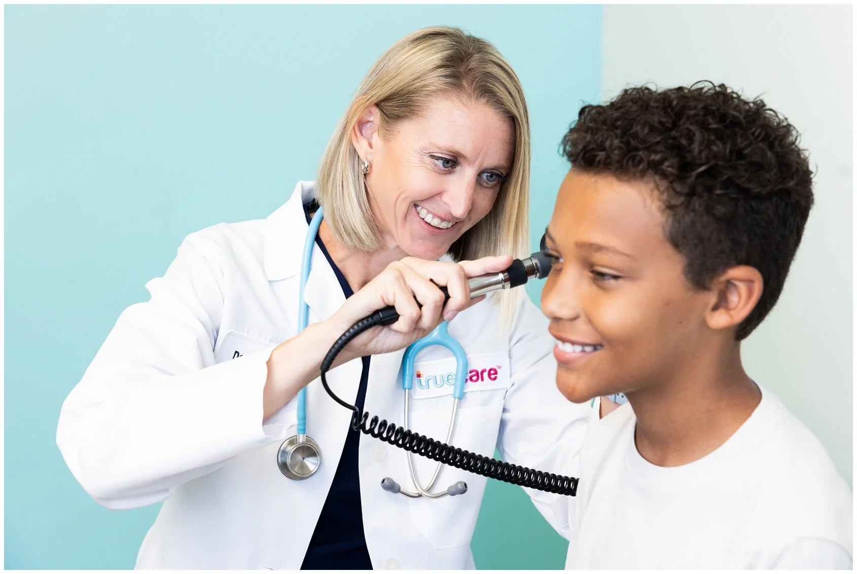 A female doctor using an otoscope to examine a young boy's ear in a medical clinic.