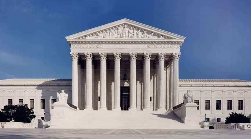 The United States Supreme Court building with white marble architecture, tall pillars, and a triangular pediment, under a blue sky.