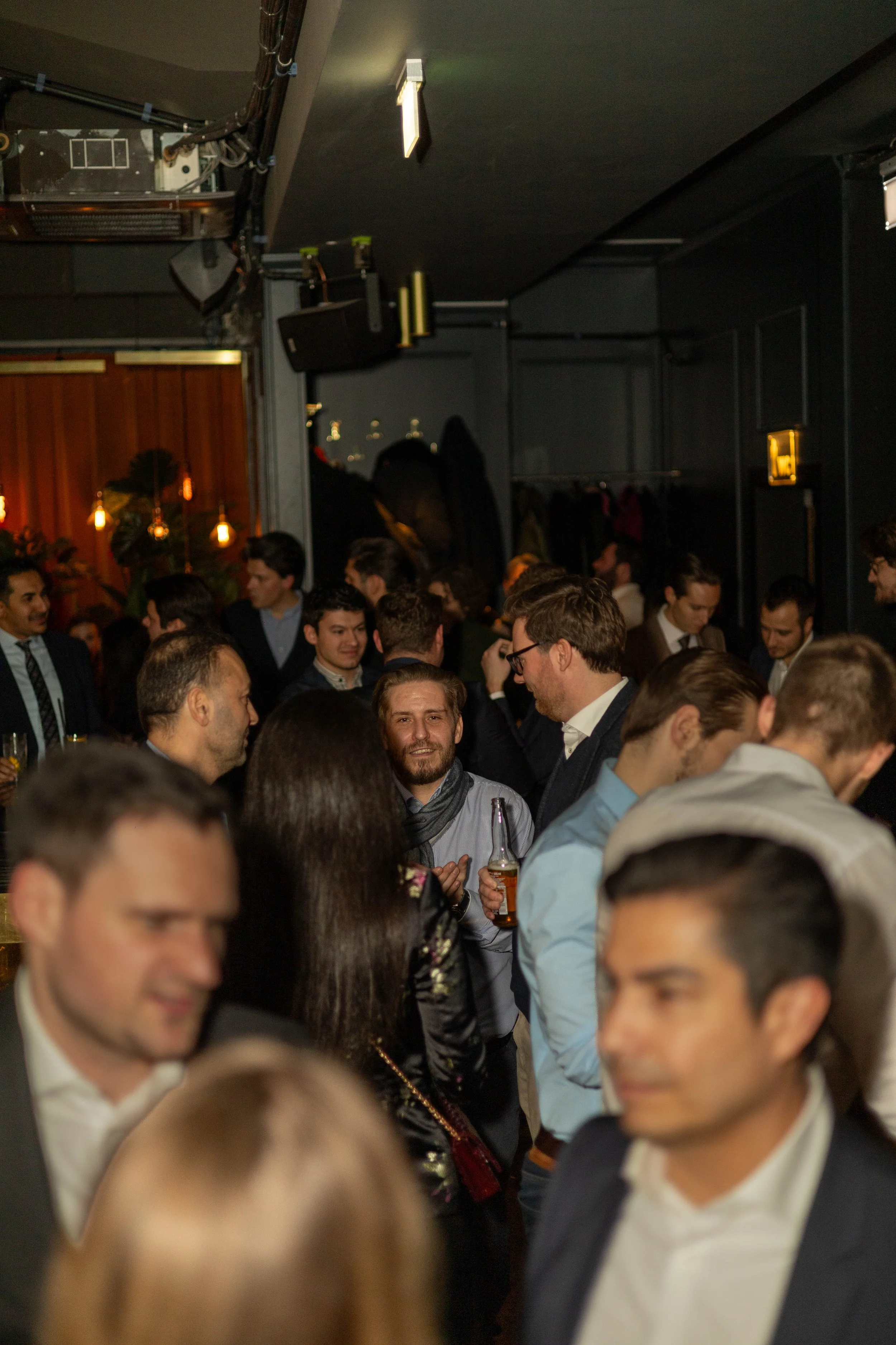 Menschen tragen formelle Kleidung auf einer Party in einem dunklen Raum mit gedämpfter Beleuchtung.