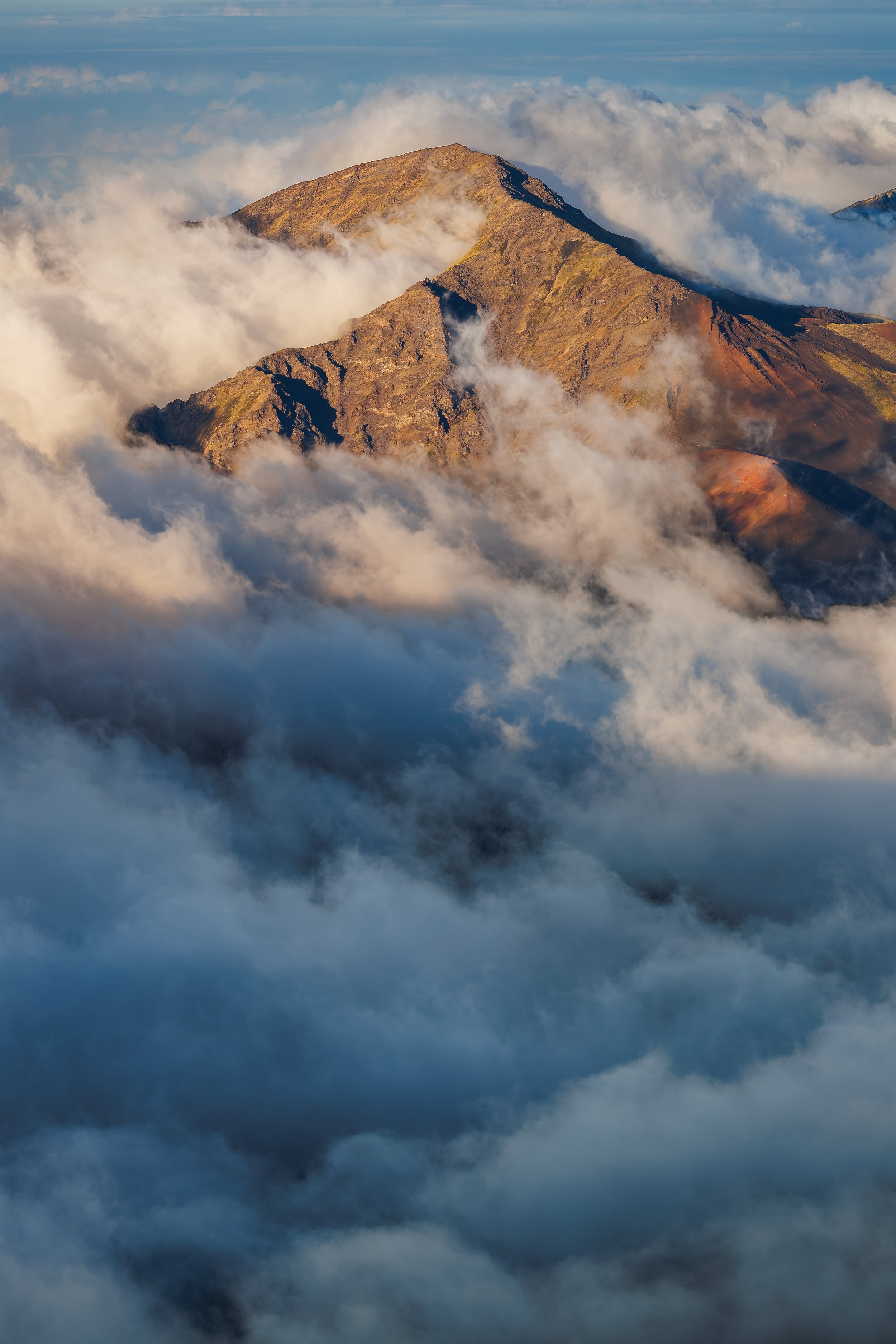 Haleakala National Park, Hawaii - Majestic mountain peak emerging above clouds at sunrise or sunset.