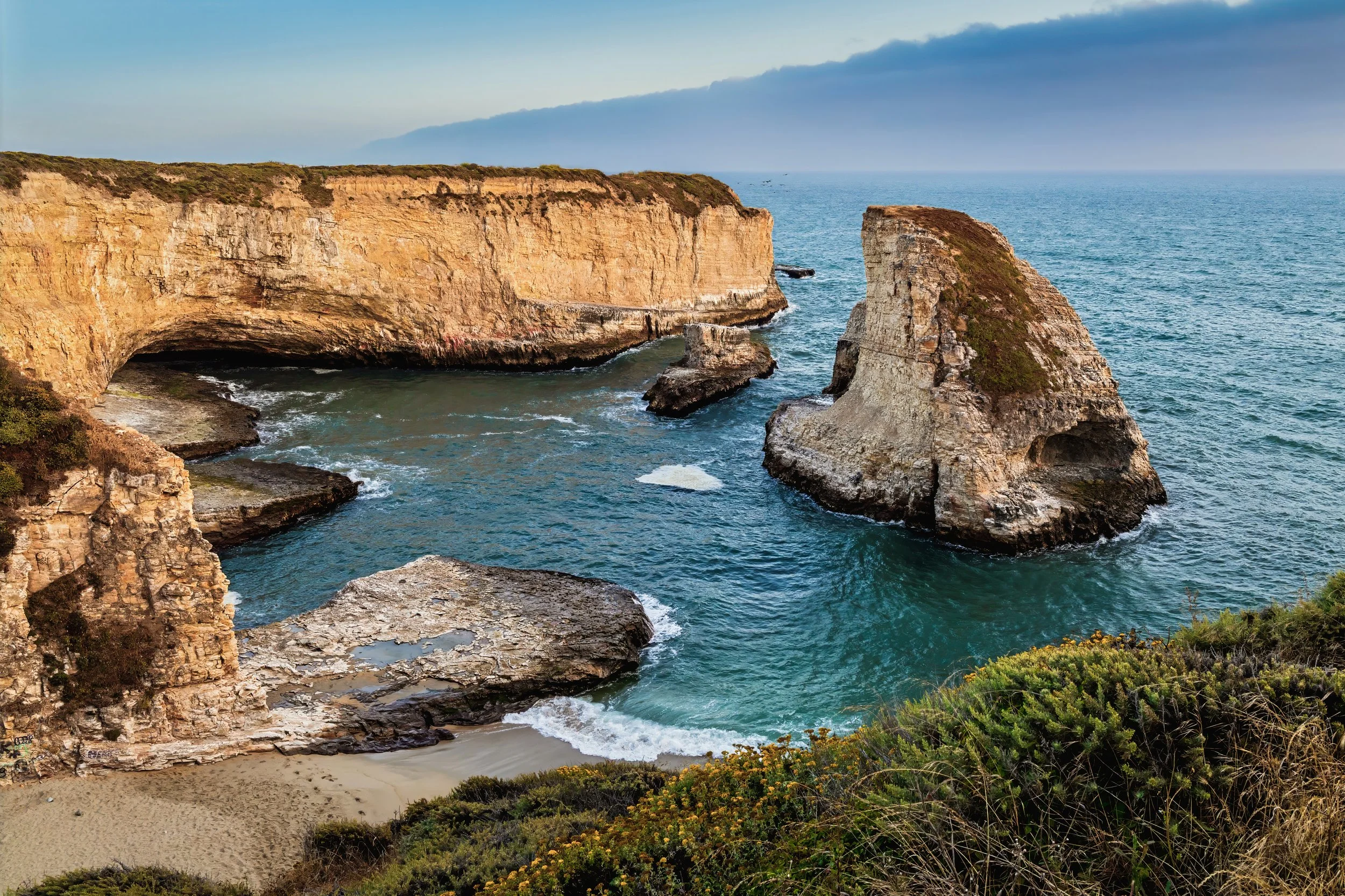Shark Fin Cove, California,cliffs along the ocean with rocks and greenery in the foreground, and a cloudy sky in the background.