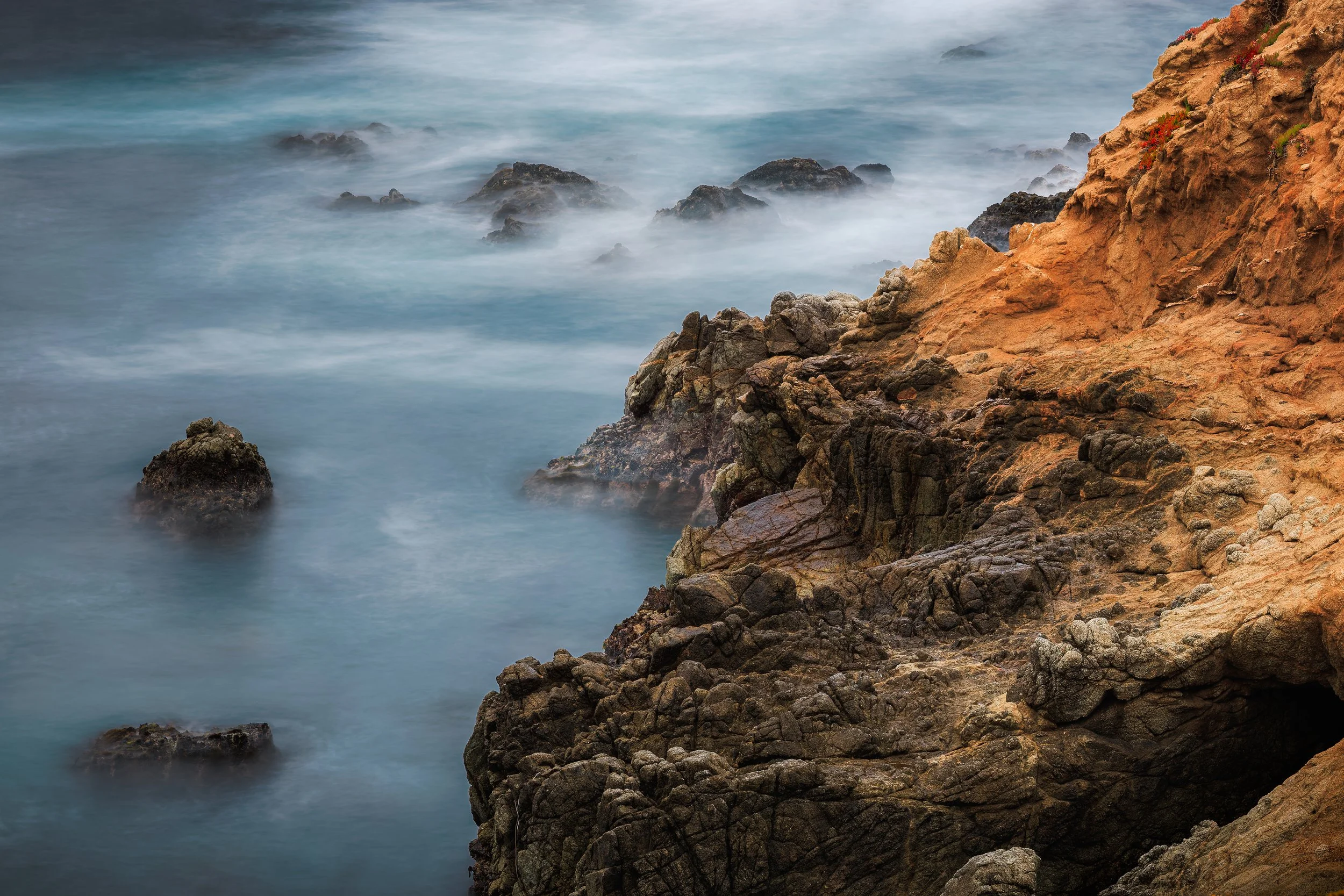 Cliffside with rocks and ocean waves crashing against the rocks.