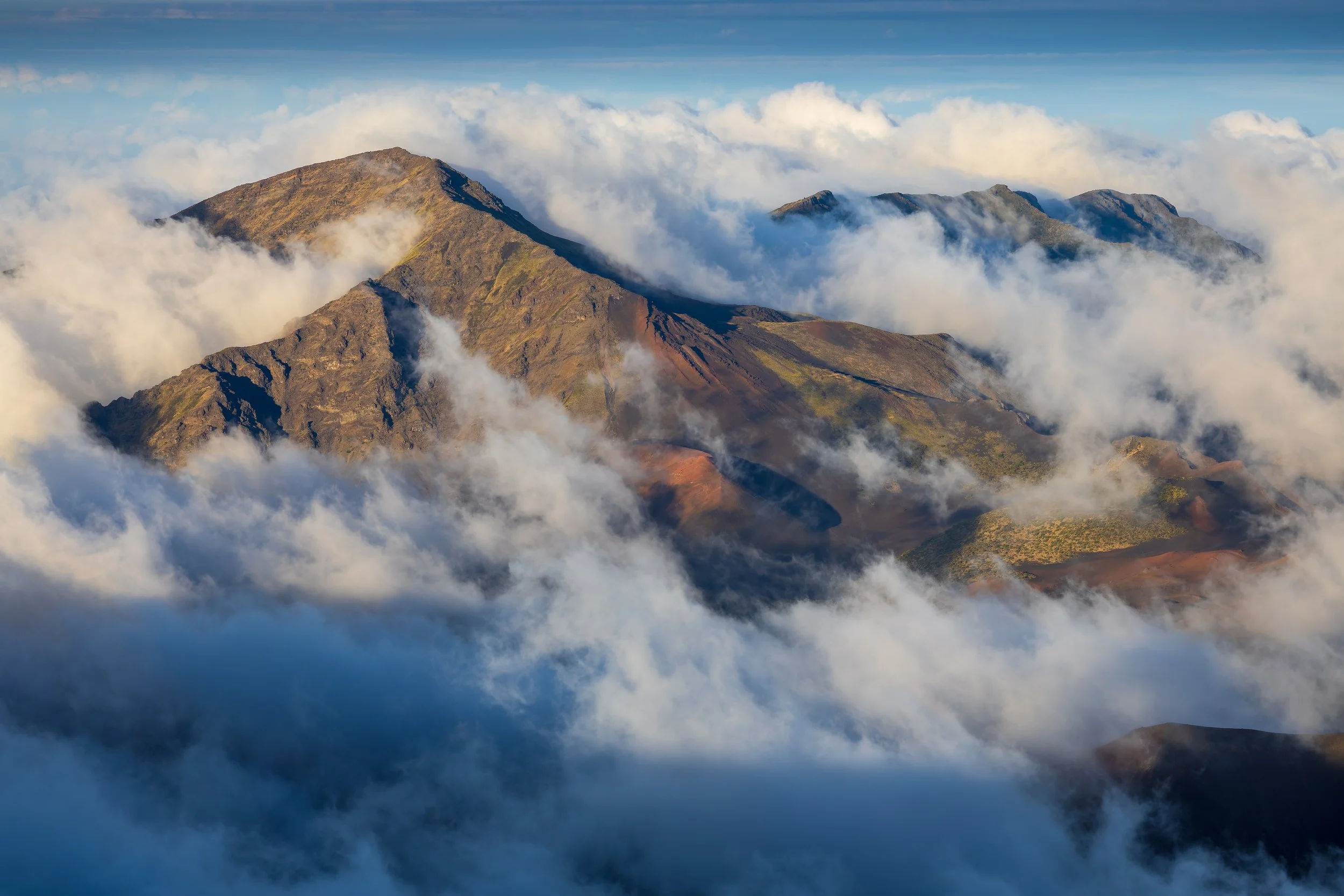 Maui, Hawaii - Haleakala National Park - A mountain range with rugged peaks partially covered by clouds, under a partly cloudy sky.