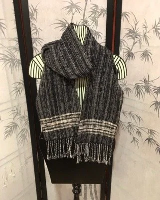 A black and gray knitted scarf with fringe at the ends, draped over a black chair, against a background of a folding screen with a bamboo-like plant pattern.