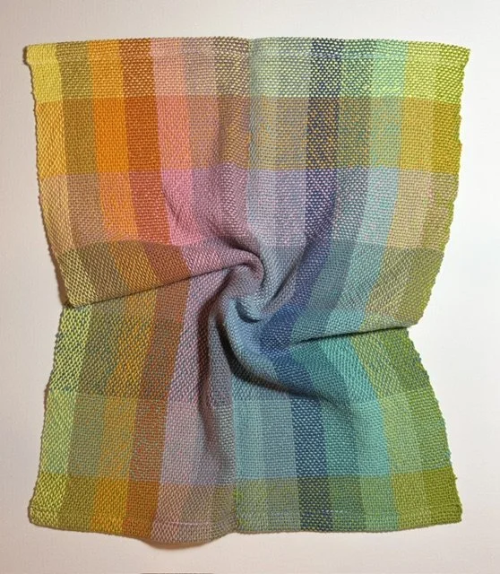 Colorful plaid fabric with a twisted and wrinkled center, featuring shades of yellow, pink, purple, blue, and green.