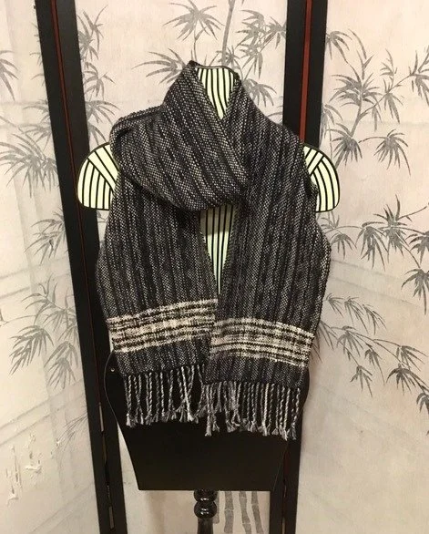 A black and white patterned scarf draped over a striped shirt on a hanger, displayed against a background with bamboo artwork.