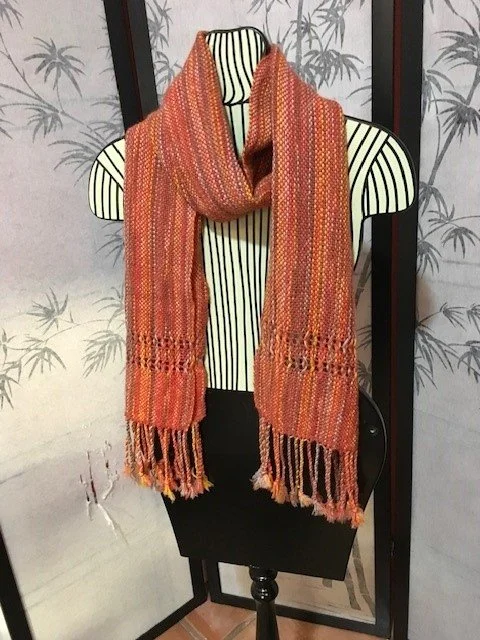 Orange patterned scarf displayed on a striped mannequin bust against a wallpapered background with palm tree designs.