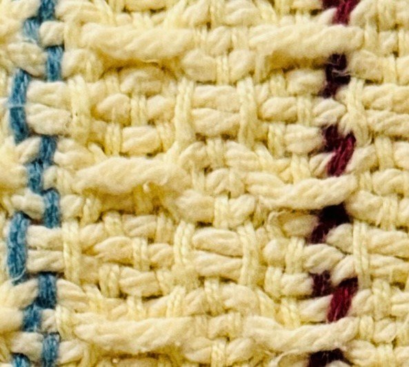 Close-up of woven fabric with beige, blue, and maroon threads.