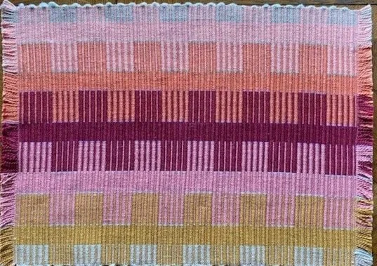 A woven rug with horizontal stripes in pink, red, purple, yellow, and light blue colors.