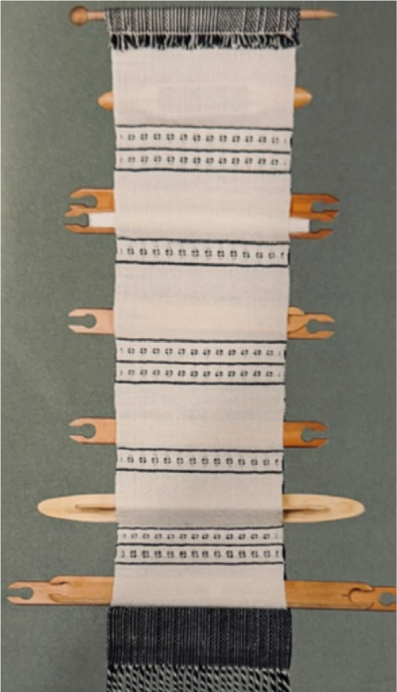 A wooden weaving loom with a piece of fabric in progress, showing a black and white striped pattern with printed technical details.