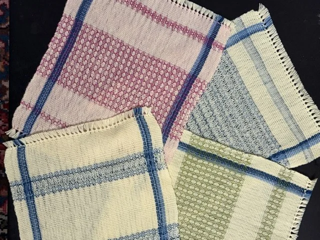 Four folded woven dish towels with striped and checkered patterns in pink, blue, green, and white, laid out on a black surface.