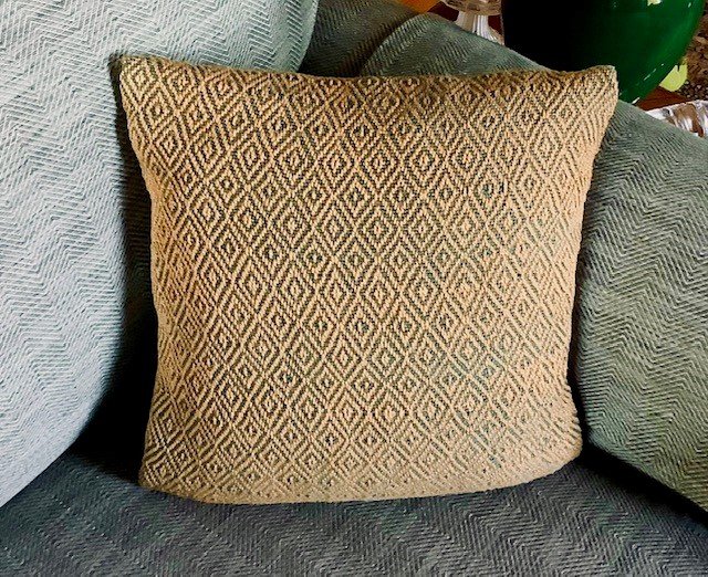 A decorative pillow with a geometric diamond pattern in cream and black, resting on a textured blue-gray sofa.