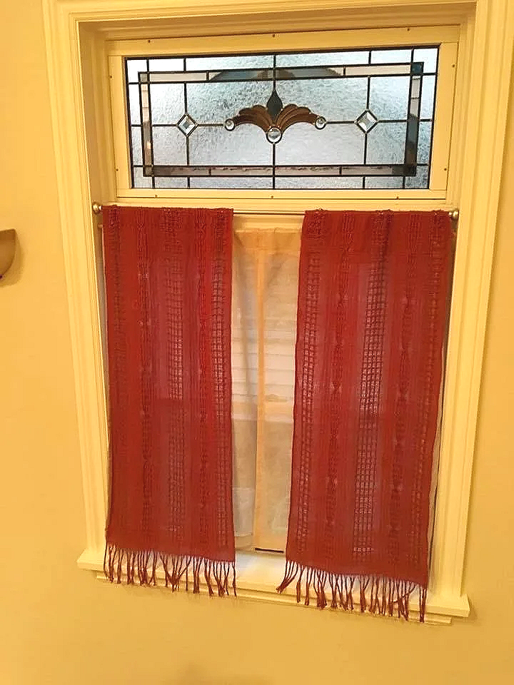 A window with decorative stained glass at the top, partially covered by red curtains with tassels.