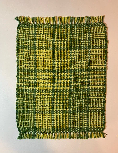 Green and yellow woven textile rug with fringed edges.