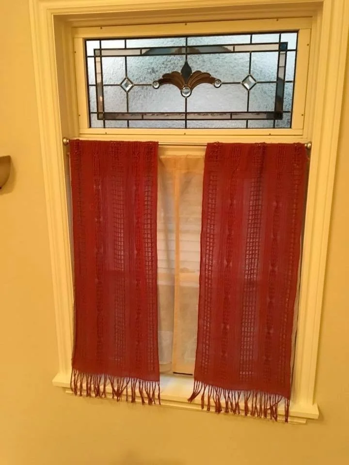 Decorative window with frosted glass and stained glass design, partially covered by red curtains with fringes.