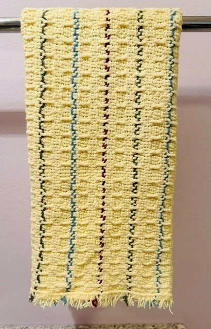Yellow towel with vertical multicolored stripes hanging on a towel rod.