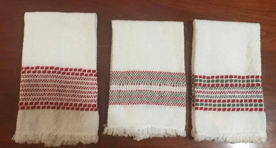 Three white hand towels with red and green decorative stripes, laid flat on a wooden surface.